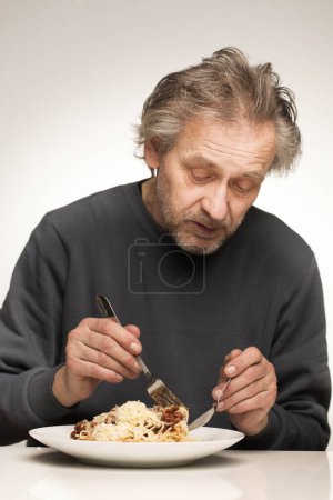 Téléchargez les photos : Un homme plus âgé mange des spaghettis à la viande hachée, tomates et fromage - en image libre de droit