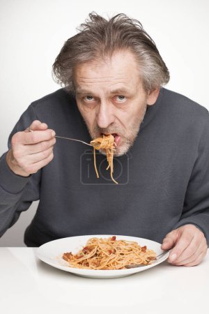 Téléchargez les photos : Un homme plus âgé mange des spaghettis à la viande hachée, tomates et fromage - en image libre de droit