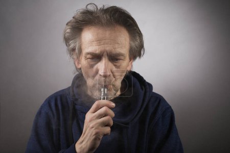 Téléchargez les photos : Homme plus âgé avec des rides sur la peau du visage fumer cigarette électronique - en image libre de droit
