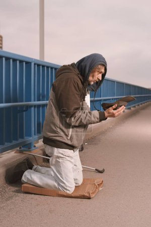 Téléchargez les photos : Un mendiant âgé sur le pont de la ville mendiant pour de l'argent - en image libre de droit