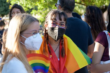 Photo for Manduria, Italy - JULY, 13, 2022 A girl with black face mask wearing a rainbow flag during the LGBT Gay Pride march. LGBTQ Pride Day Celebrations in the street - Royalty Free Image