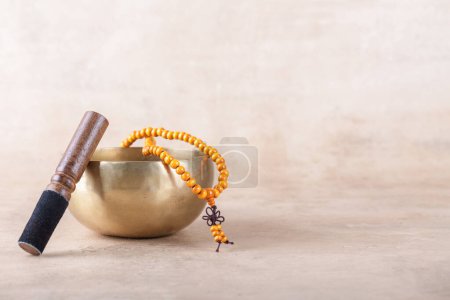 Photo for Tibetan singing bowl with stick, mala beads strands used during mantra meditations on beige stone background. Sound healing music instruments for meditation, relaxation, yoga, massage, mental health - Royalty Free Image