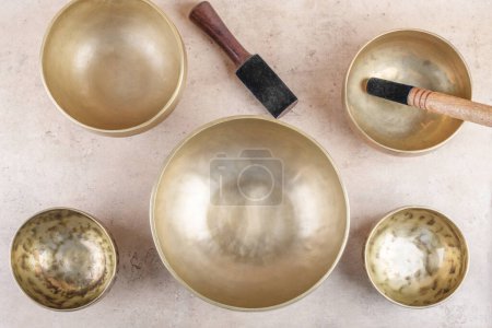 Photo for Tibetan singing bowls with stick used during mantra meditations on beige stone background, top view, flat lay. Sound healing music instruments for meditation, relaxation, yoga, massage, mental health - Royalty Free Image