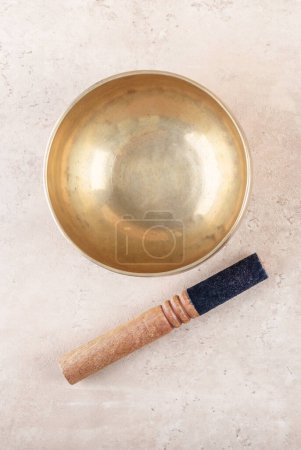 Photo for Tibetan singing bowl with stick used during mantra meditations on beige stone background, top view, flat lay. Sound healing music instruments for meditation, relaxation, yoga, massage, mental health - Royalty Free Image
