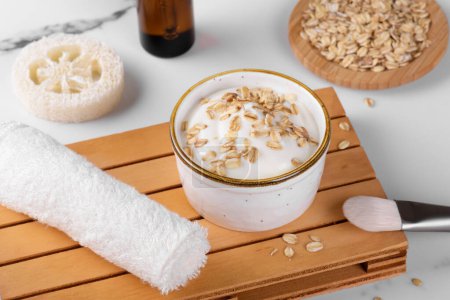 Photo for Homemade facial mask or creamy scrub with cereal, made of yogurt and oats flake, home spa cosmetics on a white marble background with natural beauty treatment ingredients and towel - Royalty Free Image