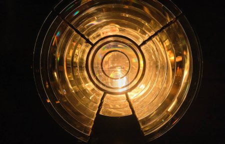Close image of the glass prism making up Fresnel lens with lights on. Used in lighthouse beacons and lanterns to concentrate light from compact lamp into revolving light beams or flashes. Round shape