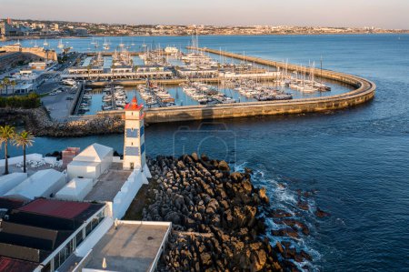 Panorama of marina and coastline of Cascais, Portugal with Santa Marta lighthouse before sunset on quiet sunny summer evening. Famous landmark by Cascais marina full of sailboats and yachts on