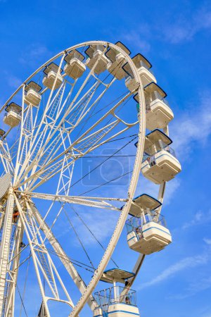 Photo for Bright white Ferris wheel on sunny day and clear blue sky with clouds, Cascais, Portugal. People enjoying rides on holiday, vertical shot, joy and leisure in sunshine. - Royalty Free Image