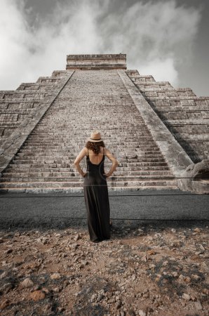 Photo for Woman wearing hat and black dress (back view, unrecognized) in front of the Chichen-Itza pyramid in Yucatan, Mexico - Royalty Free Image