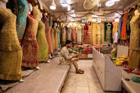 Téléchargez les photos : Pakistani man selling colorful fabric and dresses on the Qissa Khwani Bazaar in Peshawar, Pakistan - en image libre de droit