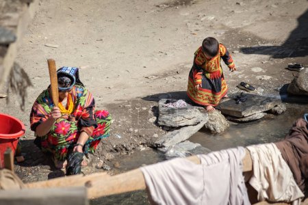 Foto de Mujer Kalash vestida con ropa tradicional haciendo la colada con su hijo cerca de su casa en la aldea Kalash, Gilgit, Pakistán - Imagen libre de derechos