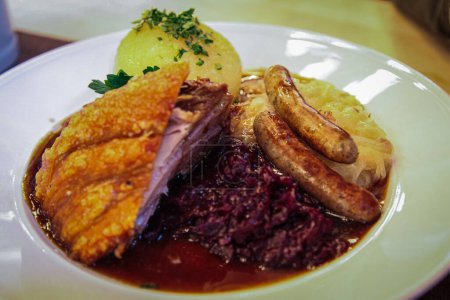 Plato de comida tradicional bávara: salchichas Nurnberg fritas, nudillos al horno, albóndigas de patata y chucrut estofado