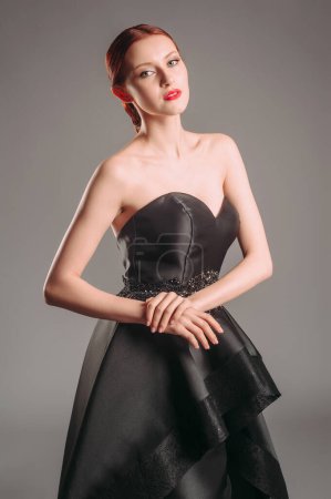 Photo for Black ball gown. Attractive ginger young woman in sleeveless evening dress on studio background. Holiday outfit. A line timeless dress with sweetheart neckline. Dramatic portrait. - Royalty Free Image