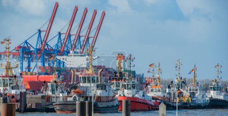 Foto de Hamburgo, Alemania - 23 de diciembre de 2023: Varios remolcadores portuarios amarrados frente a la terminal de contenedores Eurogate Burchardkai en Hamburgo - Imagen libre de derechos