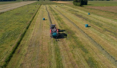 Black tractor with a red straw chamber press during the straw harvest on a mown field