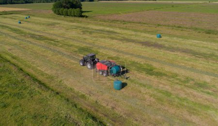 Tractor negro con una prensa de cámara de paja roja durante la cosecha de paja en un campo segado