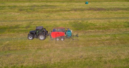 Tracteur noir avec une presse à chambre de paille rouge pendant la récolte de paille sur un champ fauché