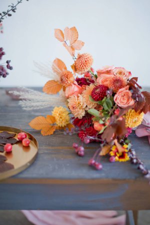 Téléchargez les photos : Beau bouquet d'automne avec des fleurs et des baies orange et rouge. Bouquet d'automne et plateau doré avec petites pommes sur une table en bois - en image libre de droit