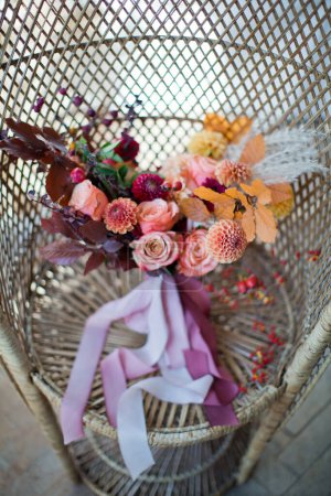 Téléchargez les photos : Beau bouquet de mariage d'automne avec des fleurs et des baies orange et rouge. Bouquet d'automne avec rubans sur une chaise de paon en rotin - en image libre de droit