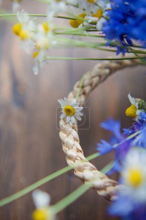 Téléchargez les photos : Fleurs de bleuet et camomille dans un sac en osier de paille sur un fond brun en bois - en image libre de droit