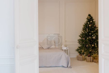 Téléchargez les photos : Chambre de Noël lumineuse avec arbre de Noël. Lit avec oreillers blancs beige i, coussins et couverture près de l'arbre de Noël - en image libre de droit