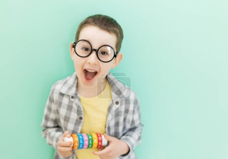 Caucasian preschool boy in eyeglasses with arithmetic math learning toy on a light green background with copy space