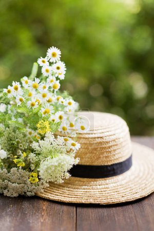 Téléchargez les photos : Chapeau de paille plaisancier et bouquet de fleurs sauvages sur une table en bois sur fond vert - en image libre de droit