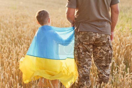 Téléchargez les photos : Military man and child with Ukraine flag in wheat field. Ukraine independence day concept. Stop war in Ukraine. Save Ukraine - en image libre de droit