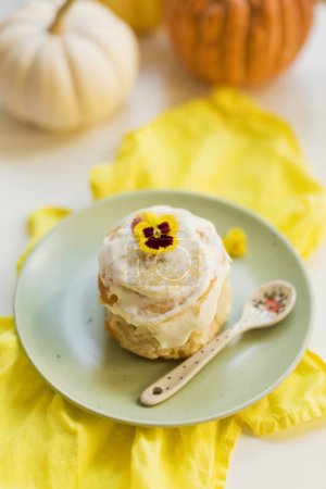 Tasty cinnamon roll bun with white cream and flower on a plate. Freshly baked pastry at home