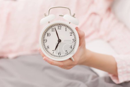 Weiße Uhr und eine Frau im rosa Pyjama, die auf dem Bett schläft