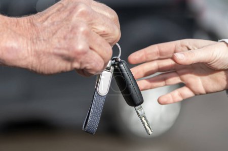A businessman hands a woman a car key in front of a blurred car