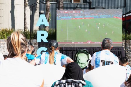 Téléchargez les photos : Les fans de football argentin assis dos à la caméra regardent la diffusion du match Argentine Pologne de la Coupe du monde de football Qatar 2022 sur un écran géant dans un environnement urbain extérieur dans la ville de Buenos Aires 30 novembre 2022. H - en image libre de droit