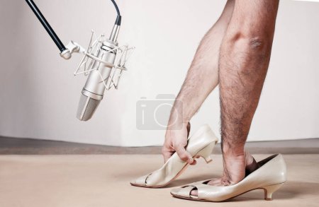 Photo for Caucasian-skinned man with beautiful bushy arms manipulates female shoes imitating steps on a wooden board in front of a silver-colored professional microphone in an interior. Close up in left side view. - Royalty Free Image