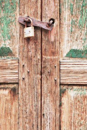 Foto de Puerta doble de madera vieja, decolorada, envejecida, seca y corroída cerrada con candado en primer plano. - Imagen libre de derechos