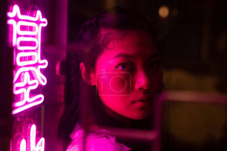Foto de Mujer asiática seria iluminada por luces de neón en la calle por la noche - Imagen libre de derechos