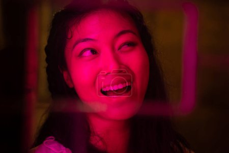Foto de Primer plano retrato de una mujer asiática feliz iluminada por luces de neón en la noche - Imagen libre de derechos