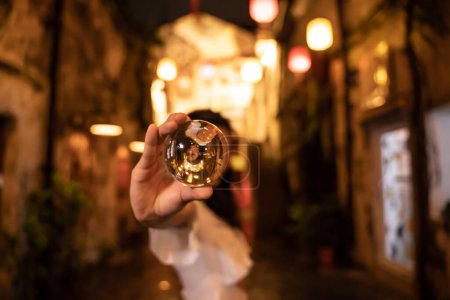 Téléchargez les photos : Femme asiatique montrant une boule de cristal dans la rue la nuit - en image libre de droit