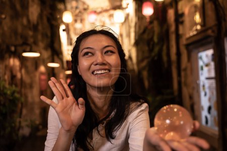 Téléchargez les photos : Drôle asiatique femme tenant une boule de cristal dans la rue la nuit - en image libre de droit