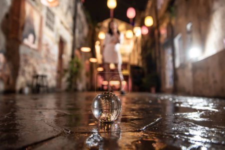Téléchargez les photos : Concentrez-vous sur une boule de cristal dans la rue à côté d'une mystérieuse femme asiatique pendant la nuit - en image libre de droit