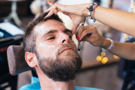 Photo for Close uo photo of a relaxed man in a hairdresser while worker shaving his beard - Royalty Free Image