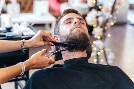 Foto de Manos de peluquero cortando la barba de un cliente en un salón de belleza - Imagen libre de derechos