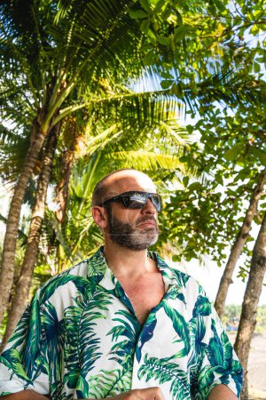 Téléchargez les photos : Portrait vertical d'un homme avec une chemise hawaïenne et des lunettes de soleil près du palmier - en image libre de droit