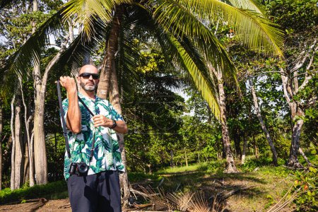 Téléchargez les photos : Photo avec espace de copie d'un homme portant un appareil photo numérique dans un environnement tropical - en image libre de droit