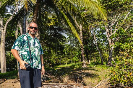 Téléchargez les photos : Photo avec espace de copie d'un homme portant un appareil photo numérique sur un environnement tropical - en image libre de droit