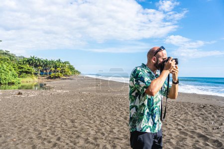 Téléchargez les photos : Photo avec espace de copie d'un homme prenant des photos avec un appareil photo numérique sur une plage tropicale - en image libre de droit