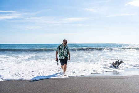 Téléchargez les photos : Photo panoramique avec espace de copie d'un homme avec une caméra marchant le long de l'eau de la plage - en image libre de droit
