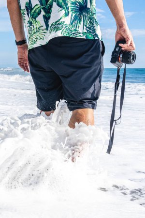 Téléchargez les photos : Homme méconnaissable avec une caméra le long de l'eau courageuse de la mer - en image libre de droit