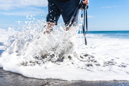 Foto de Foto recortada con espacio de copia de las olas salpicando a un hombre irreconocible con una cámara frente al mar - Imagen libre de derechos