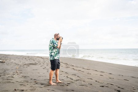 Téléchargez les photos : Photo avec espace de copie d'un homme prenant des photos avec un appareil photo numérique sur une plage de sable - en image libre de droit