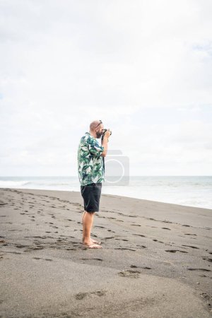 Téléchargez les photos : Photo avec espace de copie d'un homme prenant des photos avec un appareil photo numérique sur une plage - en image libre de droit